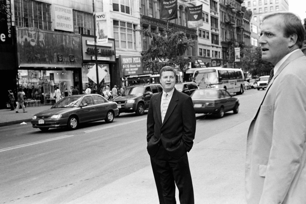 Black and white photo of two men who look like they may be looking for a cab in NYC.